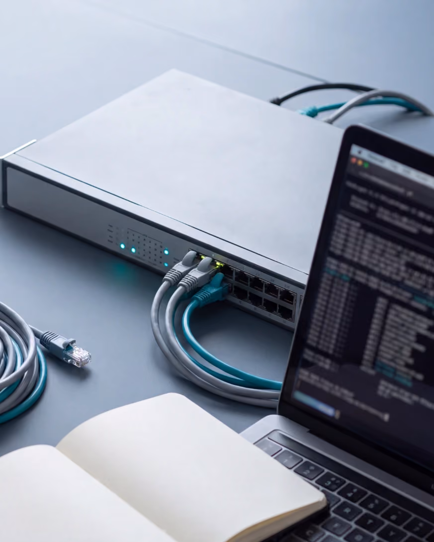 A network switch with patch cables, a laptop and a notebook on a desk